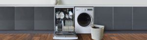 A fully loaded dishwasher in a kitchen next to a washing machine with a laundry basket placed infront